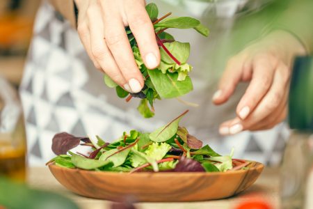 Woman putting a mix of salad on a wooden plate. Close up view.